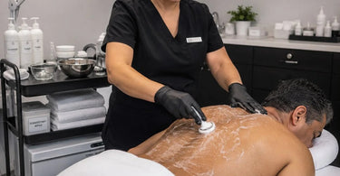 A comprehensive and efficient back facial setup featuring a professional massage table, a fully-stocked spa cart, and a facial steamer.