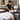 Professional spa therapist preparing a fresh towel rotation with clean white linens, a commercial towel steamer, and organized storage shelves in a busy massage treatment room