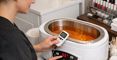 A professional therapist checking the digital temperature display on a modern paraffin wax bath unit to ensure accurate calibration for a spa treatment.