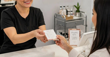 A smiling esthetician waves goodbye to a happy client in a serene spa setting