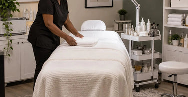 Professional spa treatment room with a facial bed, rolling trolley, LED magnifying lamp, and organized product storage for esthetician services