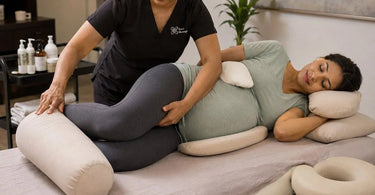 A serene spa treatment room setup for prenatal massage, featuring a massage table with supportive bolsters and pillows, soft ambient lighting, and pregnancy-safe products.