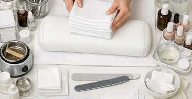 Stack of pristine, premium white facial bed linens and soft spa towels neatly folded on a wooden shelf in a professional spa treatment room.