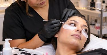 Professional lash and brow technician working carefully near a client's eyes during a salon beauty treatment, illustrating safe head positioning and client communication