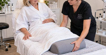 Massage therapist adjusting a bolster under a client's knees on a professional massage table to improve comfort during a spa treatment