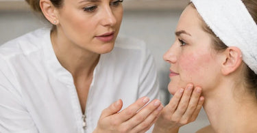 Esthetician examining client's skin with magnifying lamp during a facial treatment consultation