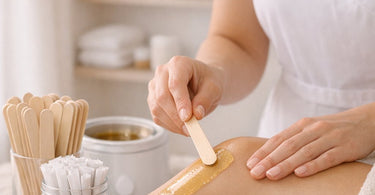 A professional esthetician holding a single-use wooden spatula, ready to apply wax from a professional wax warmer, emphasizing no-double-dipping hygiene practices in a modern spa setting.