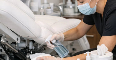 Technician inspecting and lubricating the hydraulic lift mechanism and electrical controls of a professional facial bed in a spa treatment room.
