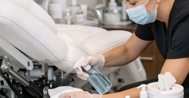 Technician inspecting and lubricating the hydraulic lift mechanism and electrical controls of a professional facial bed in a spa treatment room.