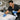 Esthetician cleaning a facial bed in a multi-bed suite with disinfectant spray and fresh linens nearby