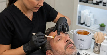 A professional esthetician precisely applying wax to a client's eyebrow to prevent spreading.
