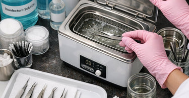 Close up of professional stainless steel eyelash extension tweezers being sanitized in a salon setup with cleaning solution and UV sterilizer