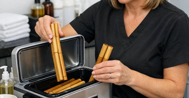 Professional bamboo massage sticks warming on a heated towel next to a bottle of massage oil on a spa table.