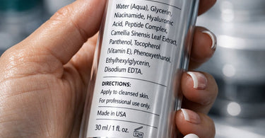 Close-up of a professional aesthetician's hands holding a skincare bottle, pointing to the ingredient label with a client looking on.