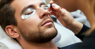 A male client receiving an eyelash tint treatment at a spa, with the technician applying tint carefully to his lashes.