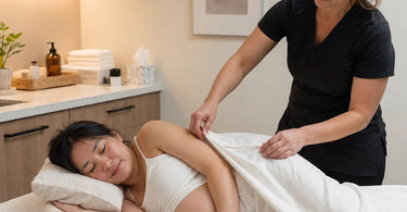 A serene prenatal massage setup showcasing a side-lying client on a massage table with bolsters and a therapist providing gentle, professional care in a calm spa environment.
