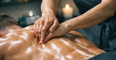 A massage therapist's hands applying cream to a client's back during a deep tissue or sports massage treatment