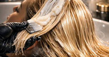 A stylist applying a thick, creamy intensive protein mask to a client's damaged hair in a professional salon setting, focusing on the mid-lengths and ends.