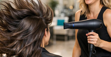 A professional stylist using a sleek new nano-ionic hair dryer to create a smooth, shiny blowout on a client with long hair.