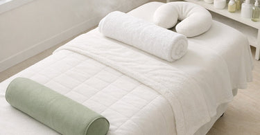 A spa professional sanitizing a massage table warmer and bolster in a clean, well-organized treatment room.