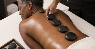 A professional massage therapist carefully selects a basalt hot stone by diameter for placement along a client's spine, symbolizing precision and therapeutic expertise in a spa setting.