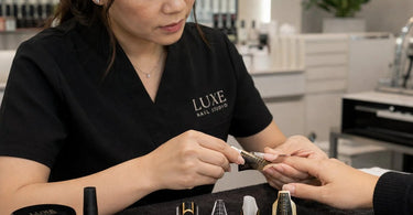 Close up of professional nail forms including paper and plastic dual forms being used to sculpt an extra-long almond shaped nail extension on a client.