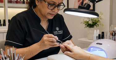 Nail technician using magnifying lamp with LED lighting for detailed nail art application in a professional salon setting.