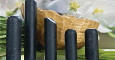 Set of 5 CoreStones massage therapy tools arranged on spa towel with warm lighting