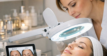 A professional esthetician using a magnifying lamp with bright LED lighting to perform a detailed skin analysis on a client in a modern spa treatment room.