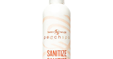 Tammy Taylor Peach Sanitize spray bottle on a clean spa towel, surrounded by peach blossoms.