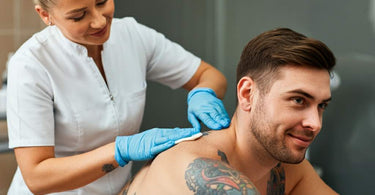 A tattooed man receiving a back wax in a professional spa setting.