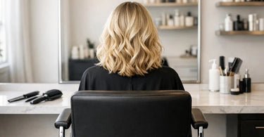 A professional hairstylist holding a large presentation mirror behind a client's chair to show the client the back of their new haircut in a bright, modern salon.