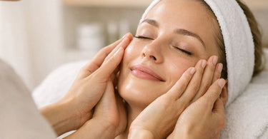 A serene spa treatment scene where a client's eyes are closed, smiling as their fingertips gently touch their own cheek, feeling the smooth results of a facial treatment, with an esthetician smiling in the background.