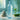 A cold bottle of water with condensation droplets sits on a spa towel next to fresh eucalyptus, representing refreshment and client care in a salon setting.