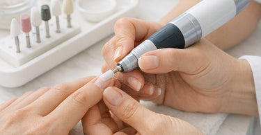 A professional nail technician safely using an electric nail file on a client's hand in a clean, modern salon setting