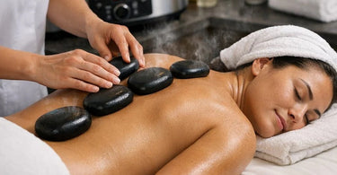 Smooth black basalt massage stones arranged on a beige towel with a white orchid and vase in a spa setting
