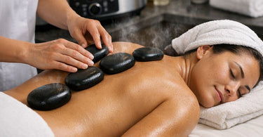 Smooth black basalt massage stones arranged on a beige towel with a white orchid and vase in a spa setting