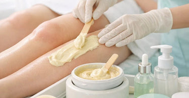 A close-up shot of a professional esthetician's hands carefully applying purple hard wax to a client's skin, highlighting the importance of product selection and technique for sensitive skin waxing services.