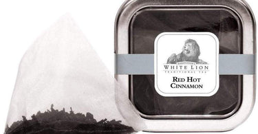 White Lion Tea Red Hot Cinnamon Black Tea tin with pyramid sachets displayed on a wooden surface with cinnamon sticks.