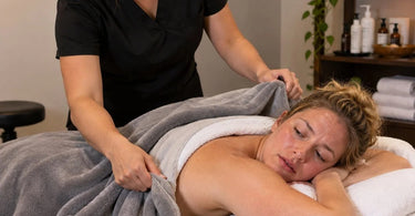 Professional massage treatment room with a client resting under a blanket, illustrating massage table warmth, layered spa bedding, and client temperature comfort during a massage.