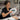 A professional esthetician's hands cleaning the glass lens of a magnifying lamp with a microfiber cloth in a spa treatment room, emphasizing the importance of lens hygiene for clear skin analysis and treatments.