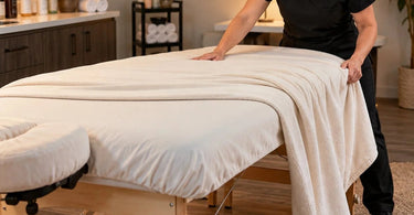 Professional massage table with a blanket sliding unevenly off one side, illustrating common spa bedding and treatment room draping problems