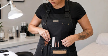 A professional nail technician wearing a stylish and functional nail tech apron with deep pockets, working on a client's nails.
