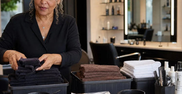 Stack of professional grey salon towels with bleach guard protection for color services, displayed on a spa counter with color supplies.