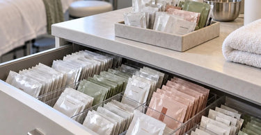 Collection of small skincare and beauty product sample packets accumulating on a professional spa treatment room counter, illustrating salon sample inventory clutter and organization challenges