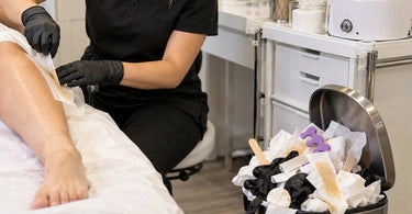 Small salon trash can filling quickly with disposable waxing and nail service supplies at a professional beauty workstation
