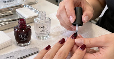 Professional nail technician applying clear top coat over colored nail polish, demonstrating how brush pressure and application technique can cause nail color to drag or smear