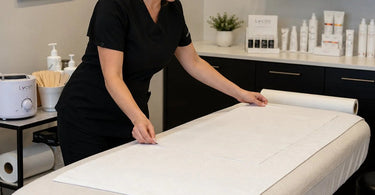 A professional waxing bed in a modern salon setting, showcasing multiple protective layers including a disposable paper cover and a fresh white towel, emphasizing hygiene and client comfort.
