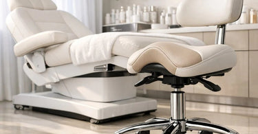 A stylish and ergonomic black esthetician's stool with a backrest, positioned next to a professional facial bed in a modern, clean spa treatment room, highlighting the importance of comfortable and supportive furniture for beauty professionals.